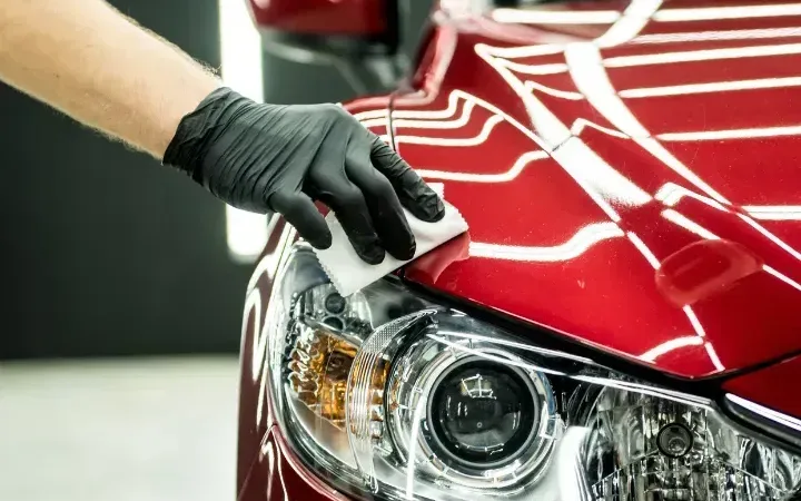 Detailer in gloves hand-finishing a red car hood during exterior detailing in Houma, LA