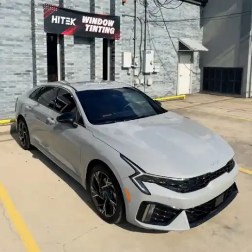 Silver Kia K5 with window tint under the HITEK Window Tinting sign in Houma, LA