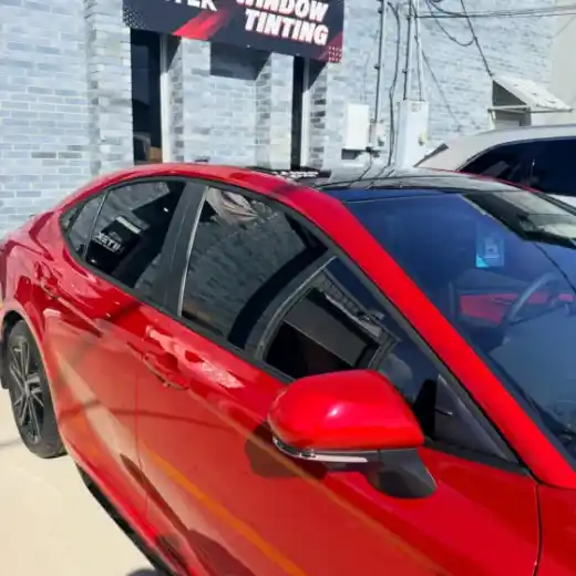 Red sedan with window tint under the HITEK Window Tinting sign in Houma, LA